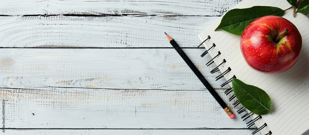 Aufkleber Back to school concept with red apple and pencil placed on a notebook against a white wooden table background creating a composition perfect for a copy space image