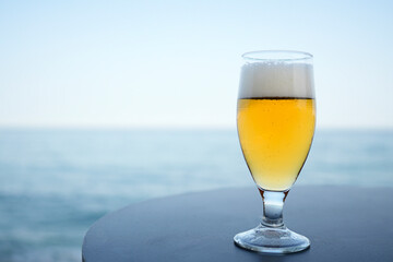 A glass of beer is sitting on a table by the ocean