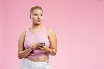 Young woman using smartphone and looking away on pink background