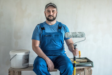 Professional worker in blue overalls is ready for wall painting. Industrial theme