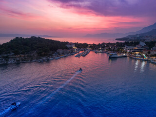 Aerial view of Makarska, Croatia at sunset, showcasing the harbor, boats, and coastline with vibrant evening colors over the Adriatic Sea.