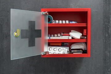 Open Red Metal Medicine Cabinet Full Of Drugs Hanging On A Dark Gray Marble Wall Background. Front View