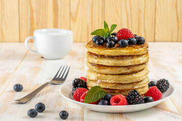 Delicious pancakes with fresh berries on white wooden table. Food concept.