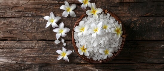 Obraz na płótnie Canvas Frangipani flowers and sea salt in a wicker basket on rustic wood ideal for a massage spa concept featuring a dark rural style with a top view and copy space image