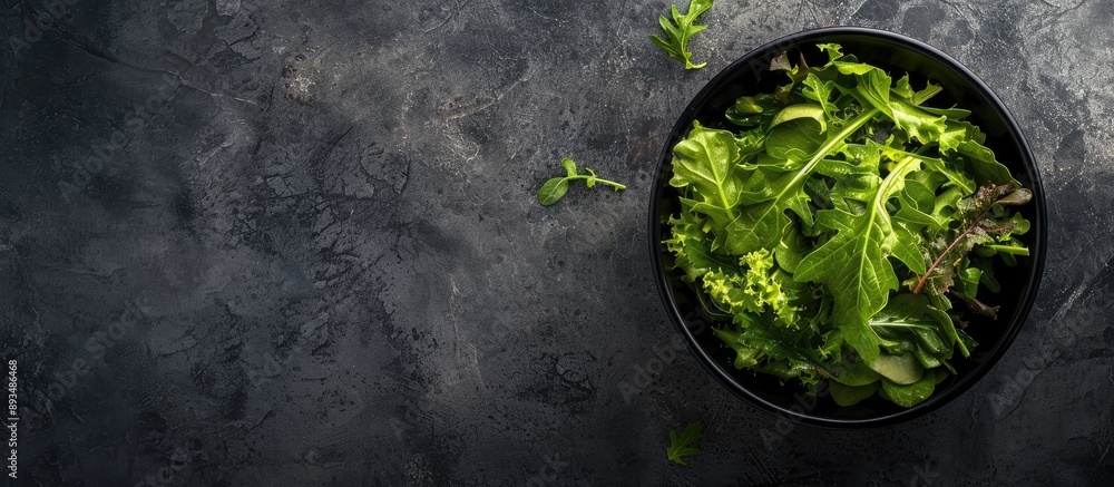 Poster Top view of salad leaves mixed in a black bowl set against a backdrop of dark slate stone or concrete with an empty space for additional content in the image