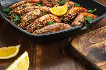 Fried shrimps on grill pan with fresh herbs and lemon slice. Seafood background.