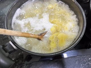 Closeup of pasta boiling in a pot with a wooden spoon.
