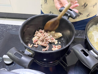Close-up of a hand stirring chopped meat in a pot on the stove.