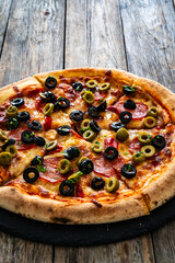 Circle pizza chorizo with black and green olives and mozzarella served on black stony board on wooden table 