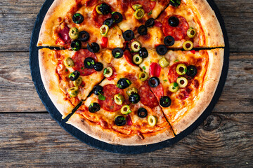 Circle pizza chorizo with black and green olives and mozzarella served on black stony board on wooden table 
