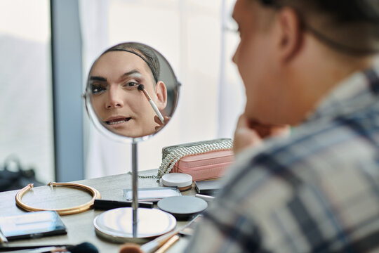A queer person applies makeup in a mirror. - Powered by Adobe