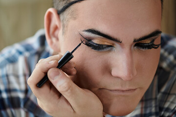 A queer person applies eyeliner with a focused expression, creating a bold look.