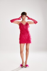 A stylish young woman poses in an elegant red feather dress against a vibrant backdrop.