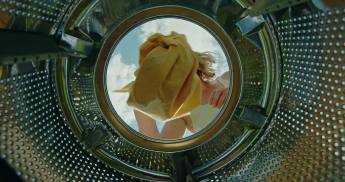 Woman putting laundry into a top-loading washing machine. Blue sky with clouds in the background