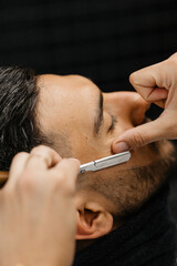 A man sitting in a barber shop getting his beard shaved by the barber