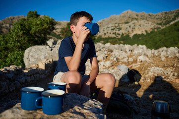 Fototapeta premium Boy enjoying a hot drink outdoors in a mountainous area on a sunny day