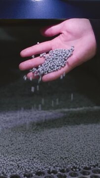 The hand touches the microplastic granules from the extruder. Plastic or polypropylene pellets on the conveyor belt of the machine. The engineer checks or inspects the raw materials for processing.