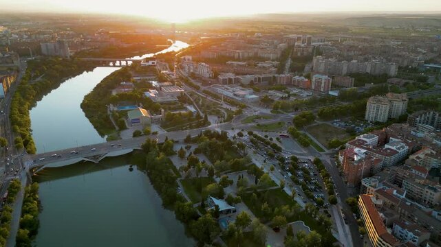 Panoramic aerial view of historic and medieval city center of Zaragoza. Drone backwards above Ebro River. Spectacular orange sunset reflecting on landscape and river. 