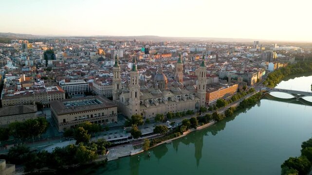 Aerial view of Zaragoza skyline. Drone going forward above Ebro River clos to Cathedral of Zaragoza and camera tilt down on roof of the cathedral. Sunset point with orange reflections. Travel.