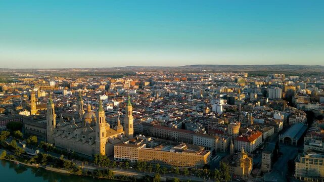 Aerial view of Zaragoza skyline. Drone going forward above Ebro River close to Cathedral of Zaragoza. Sunset point with orange reflections. Travel destination in Aragon - Spain