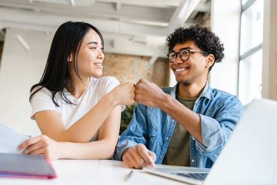 Happy colleagues business partners friends college students classmates giving fist bump while working studding doing home work create start up project together at the working desk in office cafe
