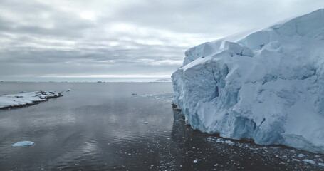Massive glacier in Antarctica peacefully floats polar ocean. Towering snow covered iceberg rises above cold, dark water. Ice wall formation under moody sky. Antarctica winter landscape panorama