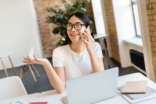 Busy young mixed-race businesswoman student marketing smm manager social media it worker freelancer inter secretary assistant talking on smart mobile phone sitting working studding at workplace area