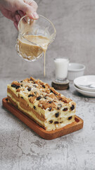 A loaf of bread pudding topped with raisins, almond and caramel sauce with hand in frame vertical