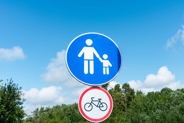 Pedestrian Sign with a sign ban on cycling. in the background blue sky and clouds. Summer day.