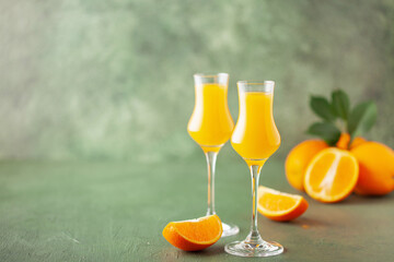 Arancello in grappas wineglass, sweet Italian orange liqueur, traditional strong alcoholic drink and oranges on the green wooden background.
