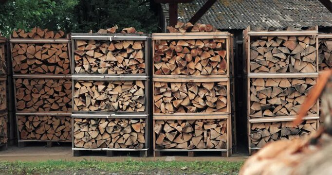 A large pile of neatly stacked firewood sits outside in a rural setting, ready for the upcoming winter season. The wood is stacked in wooden crates and is ready to be used for warmth and cooking