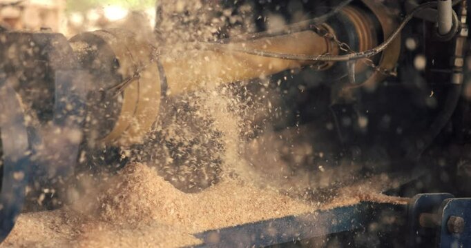 The close-up view captures the wood chipper in action, revealing a yellow spinning drum that shreds wood into fine shavings. A large pile of wood chips builds up on the ground below the machine