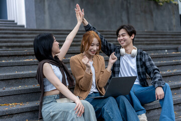 Three young people are sitting on steps, one of them holding a laptop