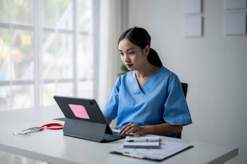 A woman in a blue scrubs is sitting at a desk with a laptop