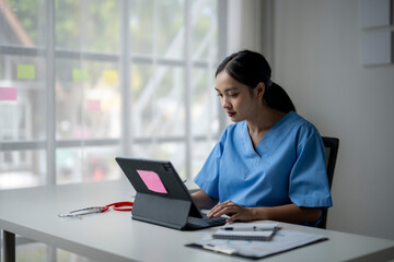 A woman in a blue scrubs is typing on a laptop
