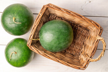 Three juicy watermelon with basket on wooden table, top view.