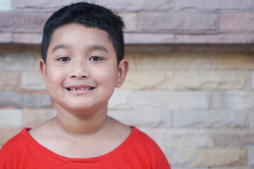 Asian boy wearing a red t-shirt, 7 years old Smiling, showing one broken upper baby tooth.