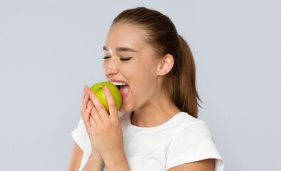 Young Lady Biting Green Apple Standing Over White Background. Healthy Snack Concept. Studio Shot, Isolated