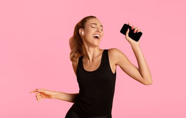 Music App. Fit Girl In Wireless Earphones Holding Mobile Phone Dancing And Listening Song Over...