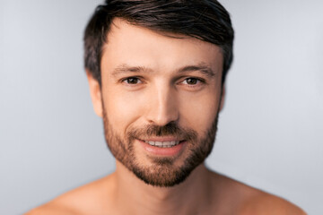 Obraz premium A close-up portrait of a man with short brown hair and a beard, smiling and looking directly at the camera.