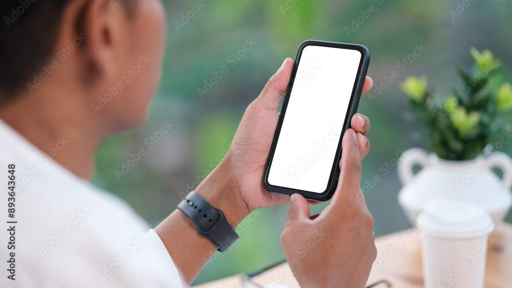 Poster rear view of young man sitting at his workspace and using smartphone. blank screen for graphics disp