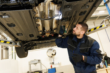 An experienced auto mechanic carefully diagnoses a car suspension with a flashlight during an insurance claim.