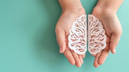 Hands hold white paper brain cutout on blue background.