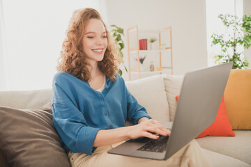 Photo of attractive trendy young woman sit sofa work netbook blue shirt move new apartment home interior indoors