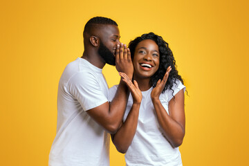 African American Man Sharing Secret With His Woman, girl is surprised, yellow studio background