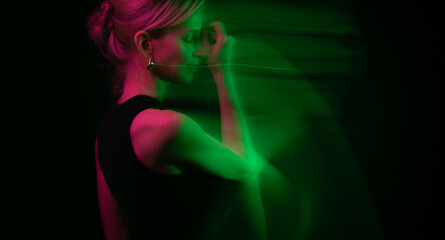 Dark colors profile portrait of blonde woman on black background. Long exposure creative artistic photography. Green and pink colors. Moody emotional composition