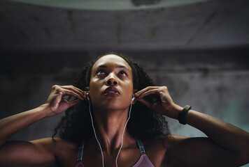 Fitness, music and face of woman at wall for commitment, determination or motivation for sport. Female athlete, earphones or serious in gym for workout, thinking or drive from favorite song on radio