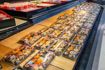 Assortment of packaged sushi trays displayed in refrigerated section at grocery store. Asian food for take away in supermarket shelf. Food retail background