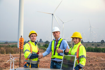 Engineer and manager in uniform shake hands and holding solar panels working teamwork in wind turbine farm, alternative renewable energy for clean power energy concept for the future.