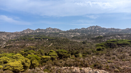 Landscape of Caprera Island in Sardinia featuring Monte Teialone in the background. The scene showcases the island's rocky hills, lush green vegetation, and clear blue sky, Mediterranean paradise